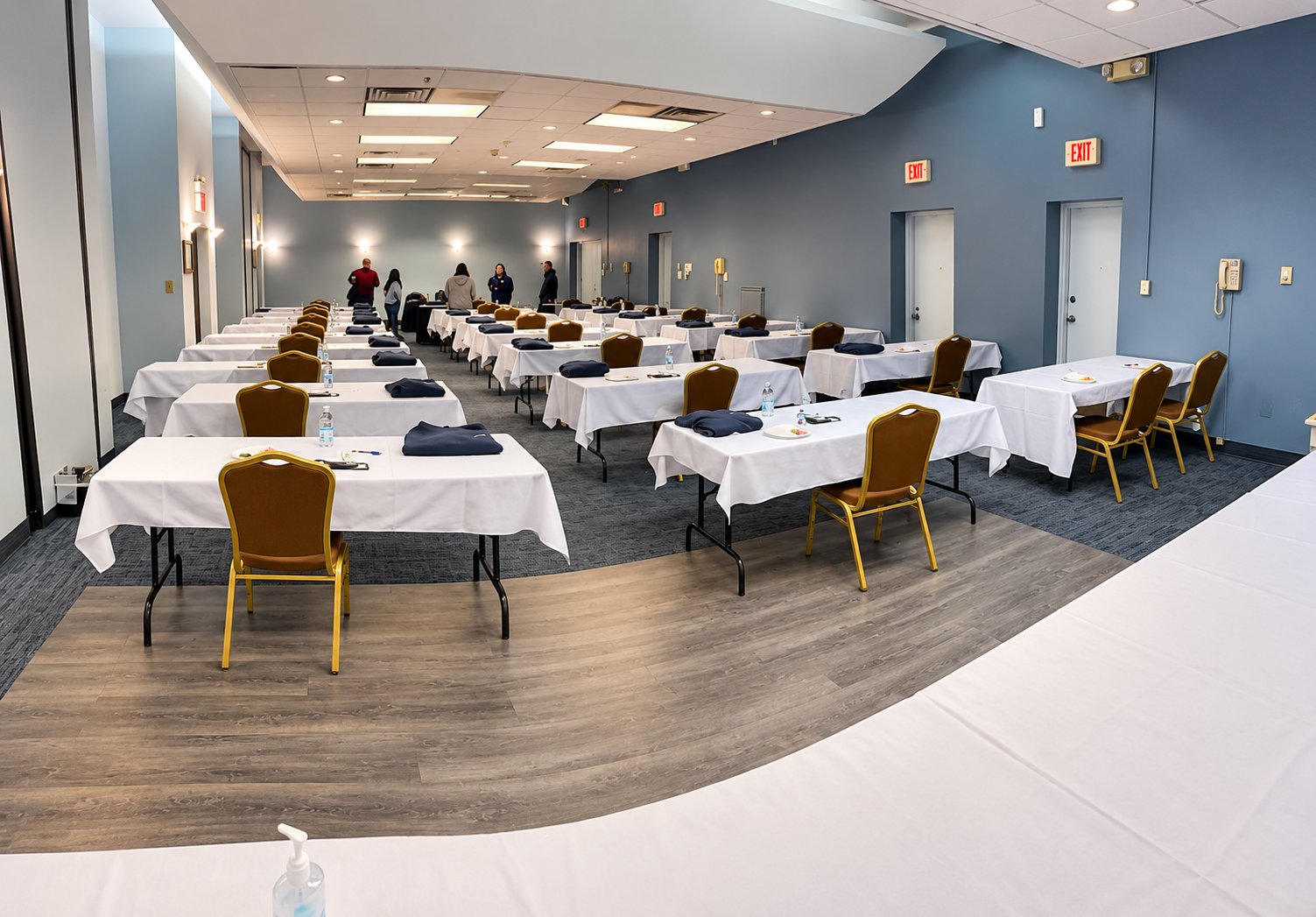 A large room set up for Choreguys onboarding day, with rows of white-covered tables, a folded navy shirt and a water bottle at every seat, and staff talking at the back