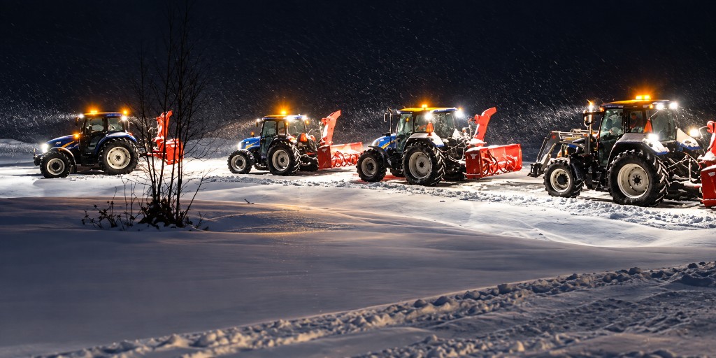 Four Choreguys tractors with red snow blowers lined up at night in falling snow